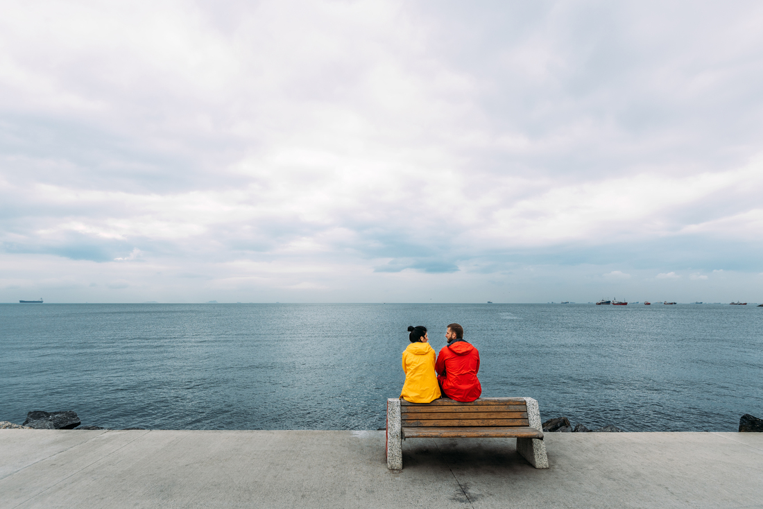 A couple sitting on a bench overlooking the oceanDescription automatically generated